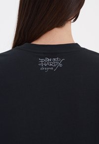 Black cotton t-shirt featuring a graphic logo in white on the upper back, with a classic crew neck and short sleeves.