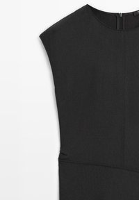 Schwarz Kleid mit strukturiertem Schulterdesign, das eine glatte Textur und sichtbare Nähte aufweist. Reißverschluss hinten; eleganter, minimalistischer Schnitt.