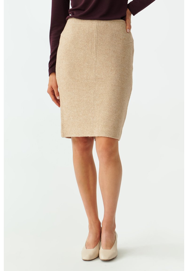 Falda de lápiz beige hecha de tela texturada, con un diseño recto, corte a la altura de la rodilla y dos bolsillos laterales. Combinada con tacones beige.