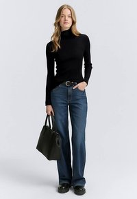 Svart ribbad polotröja kombinerad med utsvängda blå denimjeans. Svart handväska med korta handtag, bärs med klumpiga svarta skor.