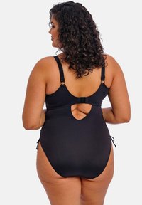 Maillot de bain noir avec bretelles réglables, détail découpé dans le dos et côtés noués. Texture lisse avec une coupe ajustée, conçu pour le confort.