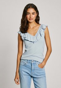 Hellblaues geripptes Oberteil mit tiefem V-Ausschnitt und geschichteten Rüschendetails am Ausschnitt, kombiniert mit hellblauen Jeans.