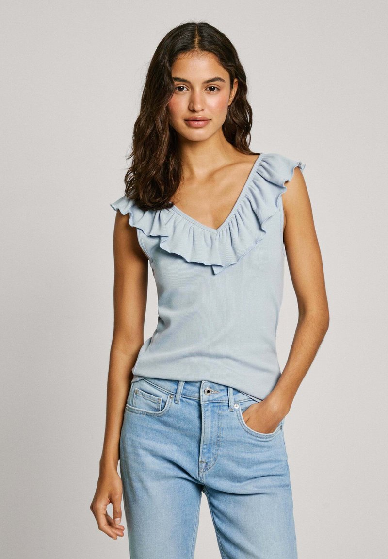 Hellblaues geripptes Oberteil mit tiefem V-Ausschnitt und geschichteten Rüschendetails am Ausschnitt, kombiniert mit hellblauen Jeans.