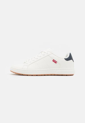 Białe skórzane sneakersy o gładkim wykończeniu, z perforowanymi detalami, granatowym akcentem na pięcie i gumową podeszwą. Czerwona metka z logo z boku.