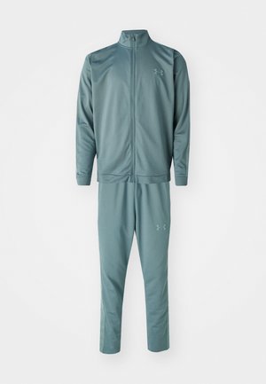 Treningsdrakt i lys teal, laget av glatt og mykt stoff. Jakken har høy krage og hel glidelås, mens buksene har sidelommer og elastisk midje.