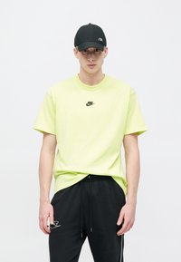 Πράσινο ασβέστη βαμβακερό μπλουζάκι με στρογγυλή λαιμόκοψη, με μικρό μαύρο λογότυπο Nike στο στήθος, σε συνδυασμό με μαύρο παντελόνι με κορδόνι στη μέση.