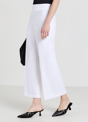 Pantaloni bianchi a gamba larga con una texture liscia, vita alta, tasche ai fianchi cucite nelle cuciture laterali, abbinati a mule nere con punta appuntita e dettagli a occhiello.