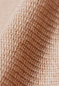 Geweven stof in een licht beige kleur, met een gestructureerd patroon van dicht gebreide steken en een zachte, pluizige uitstraling.