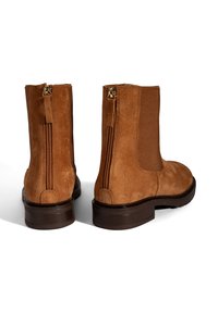 Bottines en suede marron avec une fermeture éclair sur le côté, un panneau élastique ribbed et une semelle en caoutchouc marron basse. Finition texturée sur l'ensemble.