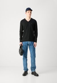 Pulover negru cu decolteuîn V, blugi din denim albastri, cizme negre și o geantă neagră. Puloverul are un mic logo pe piept; design simplu.