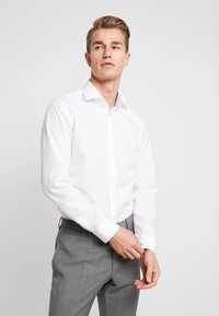 Witte overhemd met een subtiele textuur, knoopsluiting aan de voorkant en lange mouwen, gecombineerd met grijze broek. Eenvoudig, klassiek ontwerp.