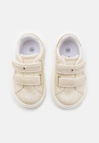 Zlatý tenký s texturovaným povrchem, vybavený dvěma suchými zipy a bílou podrážkou. Velikost 20 označena uvnitř boty.