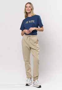 Marinblå T-shirt med "HOPE"-grafik i guld, kombinerad med beigea sweatpants med resår i midjan och vid bensluten, bärs med gråa sneakers.