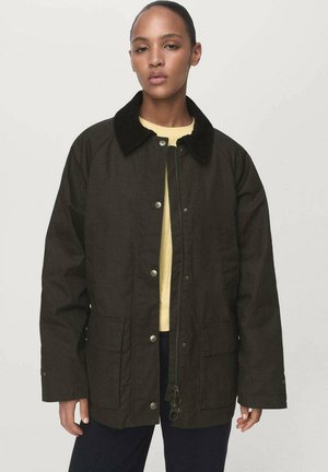 Bruine utility jack met een zwarte corduroy kraag, drukknoopjes en twee voorkruiszakken. Draag het over een gele trui. Eenvoudig ontwerp.