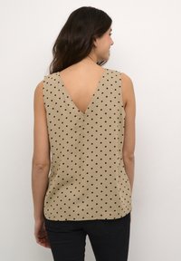 Top sans manches beige avec un dos en V, orné de pois noirs sur toute sa surface. Fabriqué en tissu lisse, il offre une coupe décontractée et un ourlet arrondi.