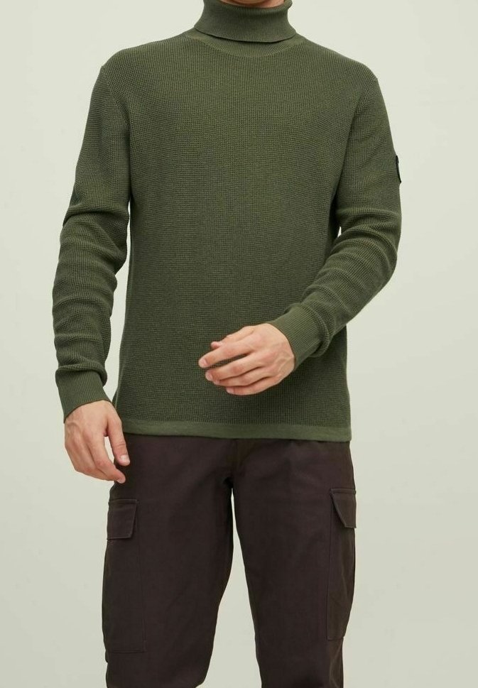 Vihreä neulottu pusero, jossa on korkeakauluksinen malli, teksturoitu kuosi, hyvin istuva siluetti ja ribbireunat, yhdistettynä tummanruskeisiin cargo-housuihin.