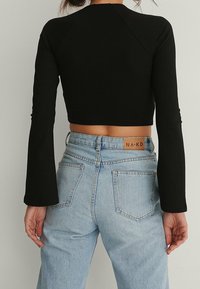 Svart långärmad kort topp med en figurnära design. Matchad med ljusblå högmidjade jeans i klassisk femfickmodell.