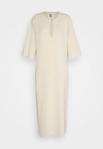 Μπεζ πλεκτό φόρεμα με κοντά μανίκια, διαθέτει στρογγυλή λαιμόκοψη και άνοιγμα σε σχήμα κλειδώματος μπροστά, διακοσμημένο με ένα μικρό κουμπί. Απλή, ευθεία γραμμή.