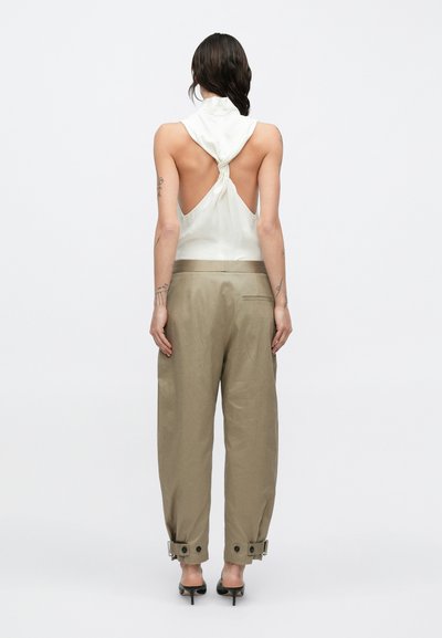 Biele tielko bez rukávov so zaväzovacím detailom na chrbte, v kombinácii s voľnými svetlohnedými nohavicami s gombíkovými ozdobami na manžetách.