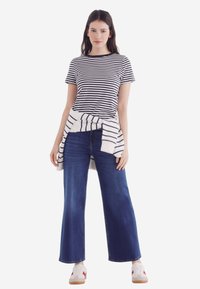 Stripet t-shirt i marineblå og hvid, parret med brede blå jeans. En hvid trøje bandt om taljen tilføjer detalje. Casual sneakers fuldender looket.
