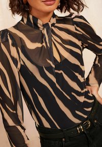 Body nero e beige trasparente con design a collo alto, maniche lunghe e apertura a chiave sul davanti, caratterizzato da un motivo a strisce simile a quello della zebra.