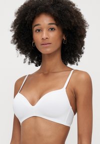 Biały, bezprzewodowy biustonosz z gładkim wykończeniem, regulowanymi cienkimi ramiączkami i dekoltem w kształcie litery V, który zapewnia bezszwową sylwetkę.