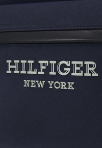 Borsa in tessuto navale con testo bianco in rilievo "HILFIGER NEW YORK" e un elegante dettaglio nero nella parte superiore. Il testo è ben visibile.
