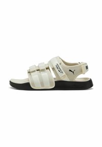 Hvid sandal med justerbare Velcro-stropper, rund tå og sort sål. Har en logo på hælen og tekstureret overdel for bedre greb.