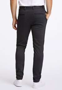 Strakzittende, donkergrijze broek van gestructureerde stof met achterzakken, gedragen met een wit T-shirt en witte sneakers.