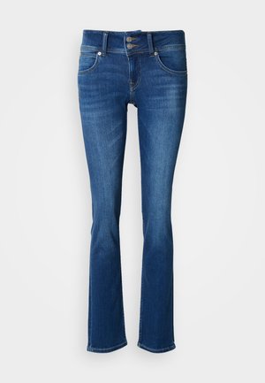 Tamsiai mėlynos spalvos džinsai iš džinsinio audinio, aptempti viršuje ir platėjančiomis apačiomis. Turi dvigubo mygtuko užsegimą, penkias kišenes ir kontrastingus siūlus.