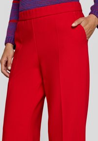 Red, tailored trousers with a smooth fabric, wide leg, and side pocket. The waistband is elasticated for comfort.