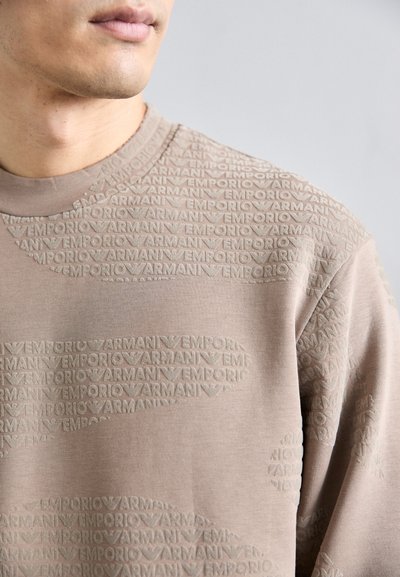 Világos taupe színű pulóver, kiemelkedő, ismétlődő logó mintázattal. Puha anyag, texturált felülettel és standard kerek nyakú kivitelben.