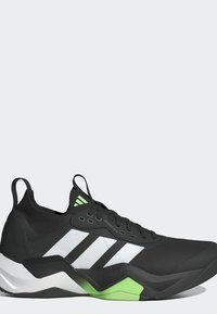 Chaussure de sport noire avec des bandes blanches, des accents verts et une semelle épaisse, avec des languettes au talon et sur la languette, présentée sur un fond uni.
