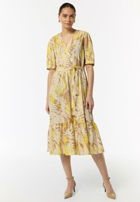 Kleid mit Blumenmuster in Gelb-, Beige- und Hellbrauntönen. V-Ausschnitt, kurze Puffärmel und ein gestufter Rüschensaum. Mit gebundenem Taillendetail.