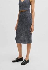 Twee-delig outfit bestaande uit een marineblauw crop top met een gestructureerd patroon en een bijpassende rok tot de knie. Draagt met zwarte instappers.