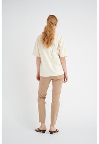 Beige kortærmet top med lige snit, parret med lysebrune slim-fit bukser og sorte hæl-sandaler. Glatte teksturer, minimalistisk design.