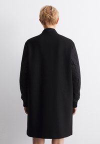 Giacca nera con corpo in lana testurizzata e maniche in tessuto trapuntato. Caratterizzata da un colletto e polsini a costine, offre un design pulito e lineare.