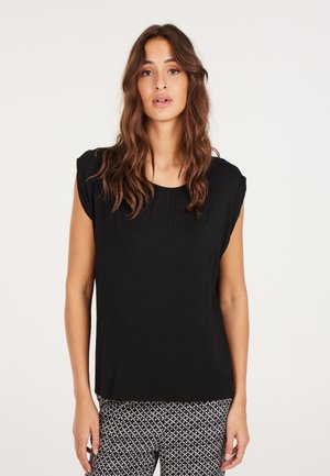 Top corto nero a maniche corte con scollatura rotonda e dettagli arricciati. Abbinato a pantaloni neri e bianchi con motivo geometrico.