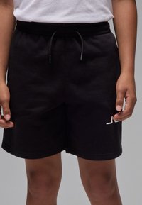 Schwarze Baumwollshorts mit elastischem Bund und Kordelzug. Auf der unteren linken Seite befindet sich ein kleines weißes Logo. Glatte Textur.