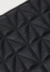 Portofel din piele neagră, cu un model capitonat în formă de diamant, textură netedă și detalii cu cusături contrastante. Formă compactă și rectangulară.