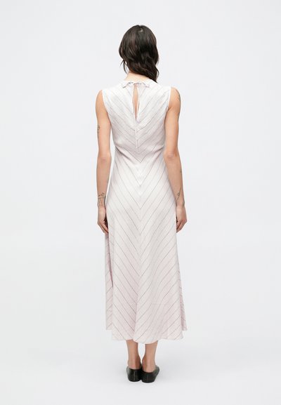 Svetloružové šaty bez rukávov so vzorom šípok, s otvorom na chrbte a voľnou áčkovou siluetou, doplnené čiernou obuvou.