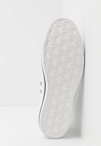 Weißer Sneaker mit einer strukturierten Gummisohle mit Schachbrettmuster, geprägt mit einem Logodetail und einem kontrastierenden schwarzen Rand entlang der Kante.