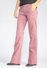 Růžové bavlněné rozšířené kalhoty se zapínáním na zip a knoflík. Disponují předními kapsami a jemnými švy. Noseny s černými vysokými botami.