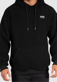 Svart fleecehoodie med en texturerad yta, justerbara dragsko, och en liten logotyp på bröstet. Ribbad muddar och nederkant.