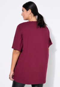 Camiseta oversized burdeos con mangas cortas, fabricada en algodón suave, que presenta un sencillo escote de cuello redondo y un corte relajado para mayor comodidad.