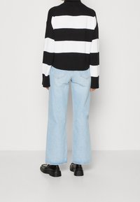 Pull en maille rayé noir et blanc associé à un jean large bleu clair et des chaussures noires, mettant en valeur la texture côtelée et une coupe décontractée.