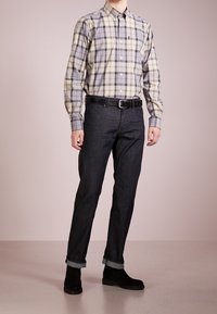 Langarmige plaid shirt in beige, grijs en blauw; met knoopsluiting bij de kraag. Combinatie met donkere spijkerbroek en zwarte enkellaarsjes.