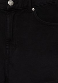 Gros plan sur un jean en denim noir montrant le bouton, le rivet, la ceinture et les détails de couture de la poche avant.
