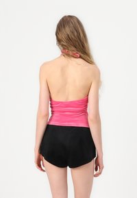 Ροζ, εφαρμοστό halter top με πτυχές στην πλάτη, συνδυασμένο με μαύρα, φαρδιά σορτς. Μαλακή υφή υφάσματος.