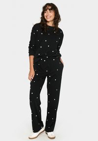 Schwarzes Loungewear-Set mit weißen Herzmustern. Das Oberteil hat lange Ärmel und einen Rundhalsausschnitt, während die Hose einen elastischen Bund hat.